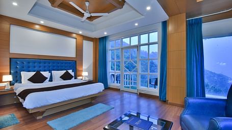 A large bed placed in front of the sofas in Luxury Room with Balcony at DLS Highland Resort and Spa, Mussoorie.